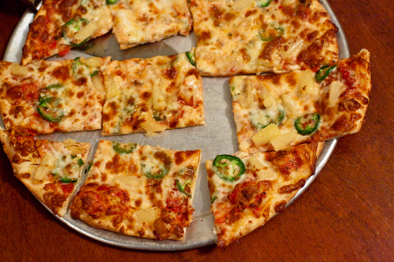 Jalepenos and pineapple top a thin crust pizza on a table at Rocco's Thin crust pizza at Rocco's editorial food photography by Jackie Alpers for a magazine feature article